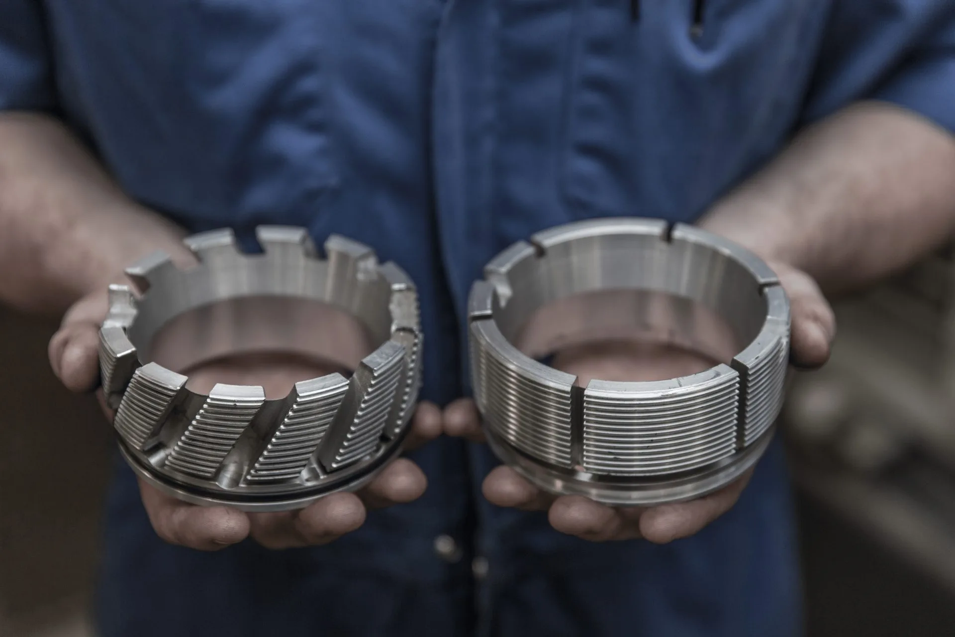 Close-up of hands holding two metal drill bits with segmented cutting edges, used for industrial drilling applications.