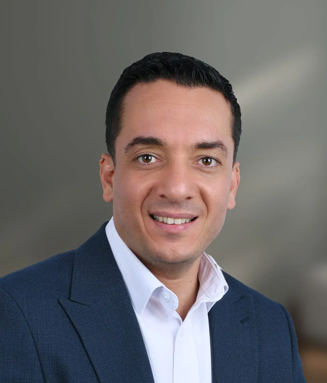 Professional headshot of Ahmed Hadi against a plain gray background.