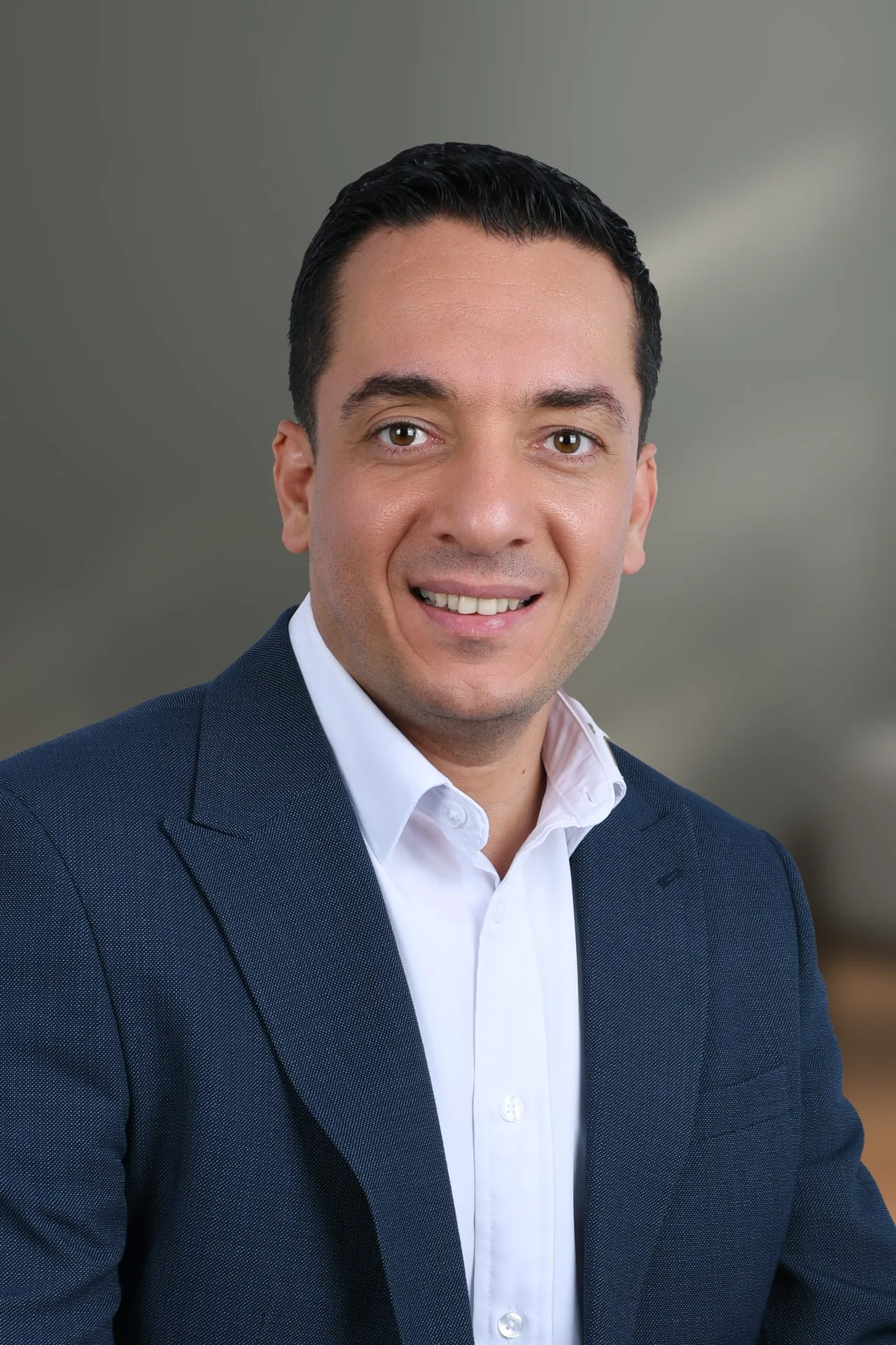 Professional headshot of Ahmed Hadi against a plain gray background.