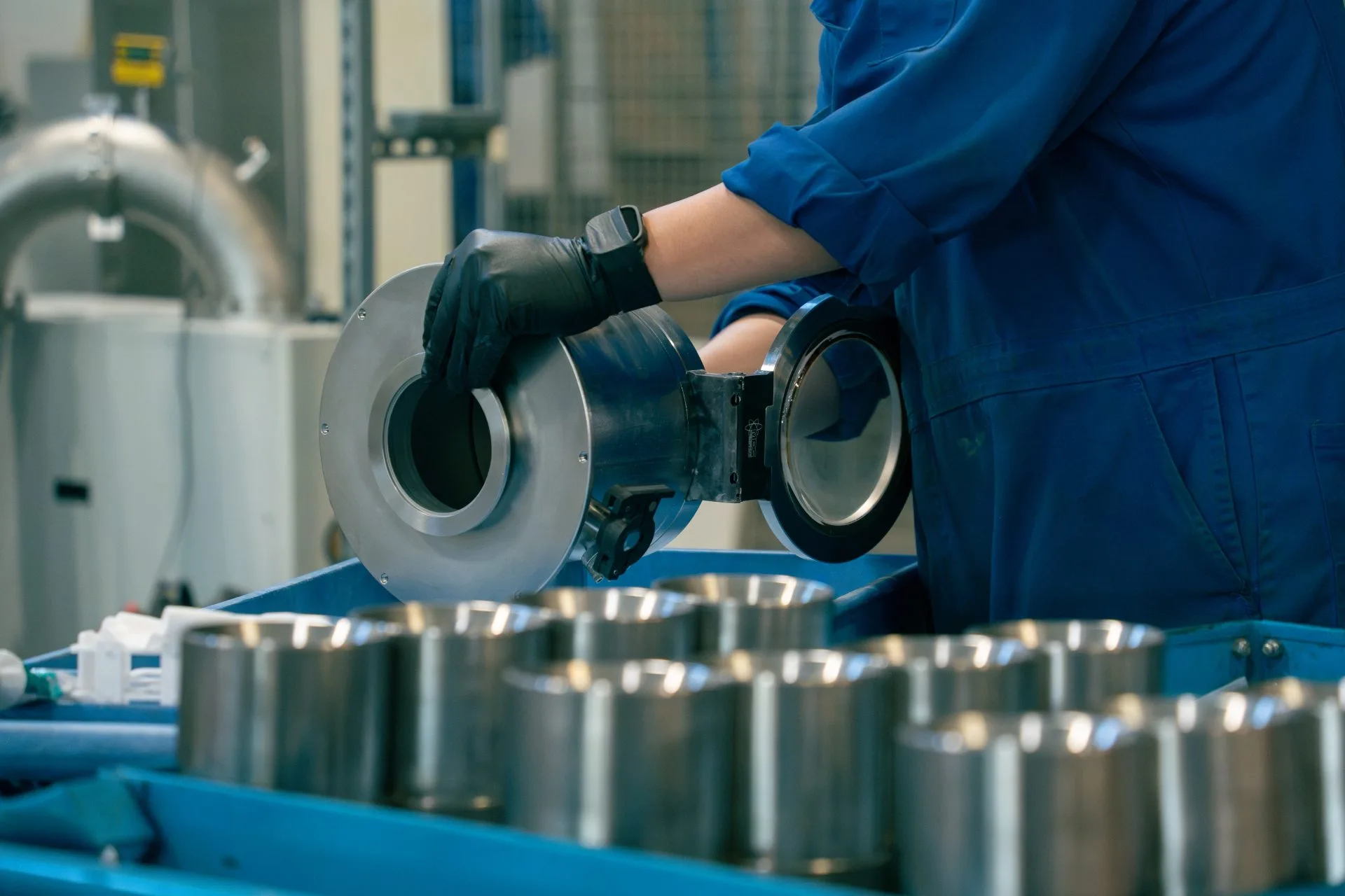 Worker wearing gloves inspecting a metal component in an industrial manufacturing facility.