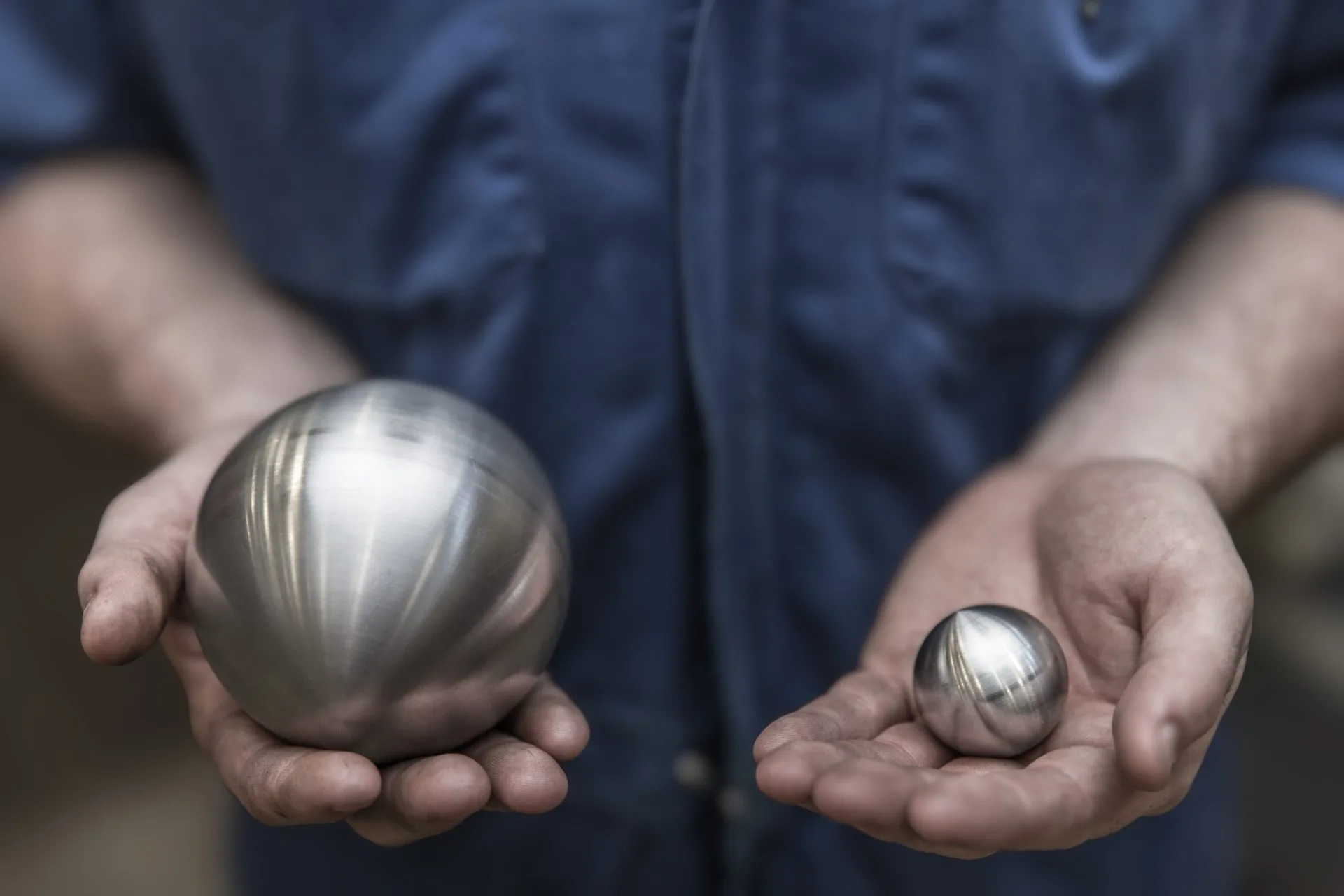 Person holding two metallic spheres of different sizes, highlighting the contrast between them.